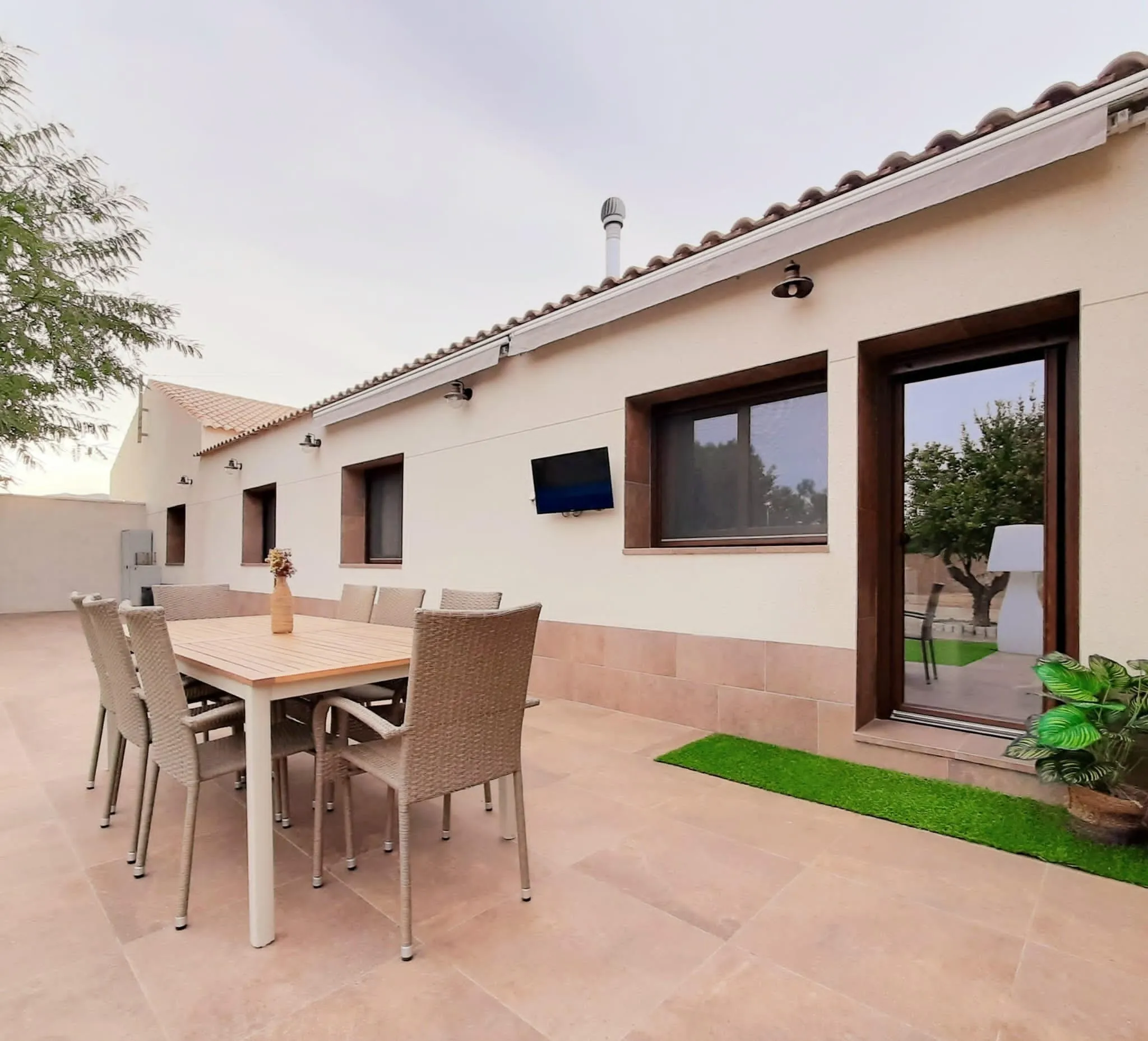 Terraza pavimentada con mesa de comedor exterior junto a la fachada blanca y la puerta acristalada
