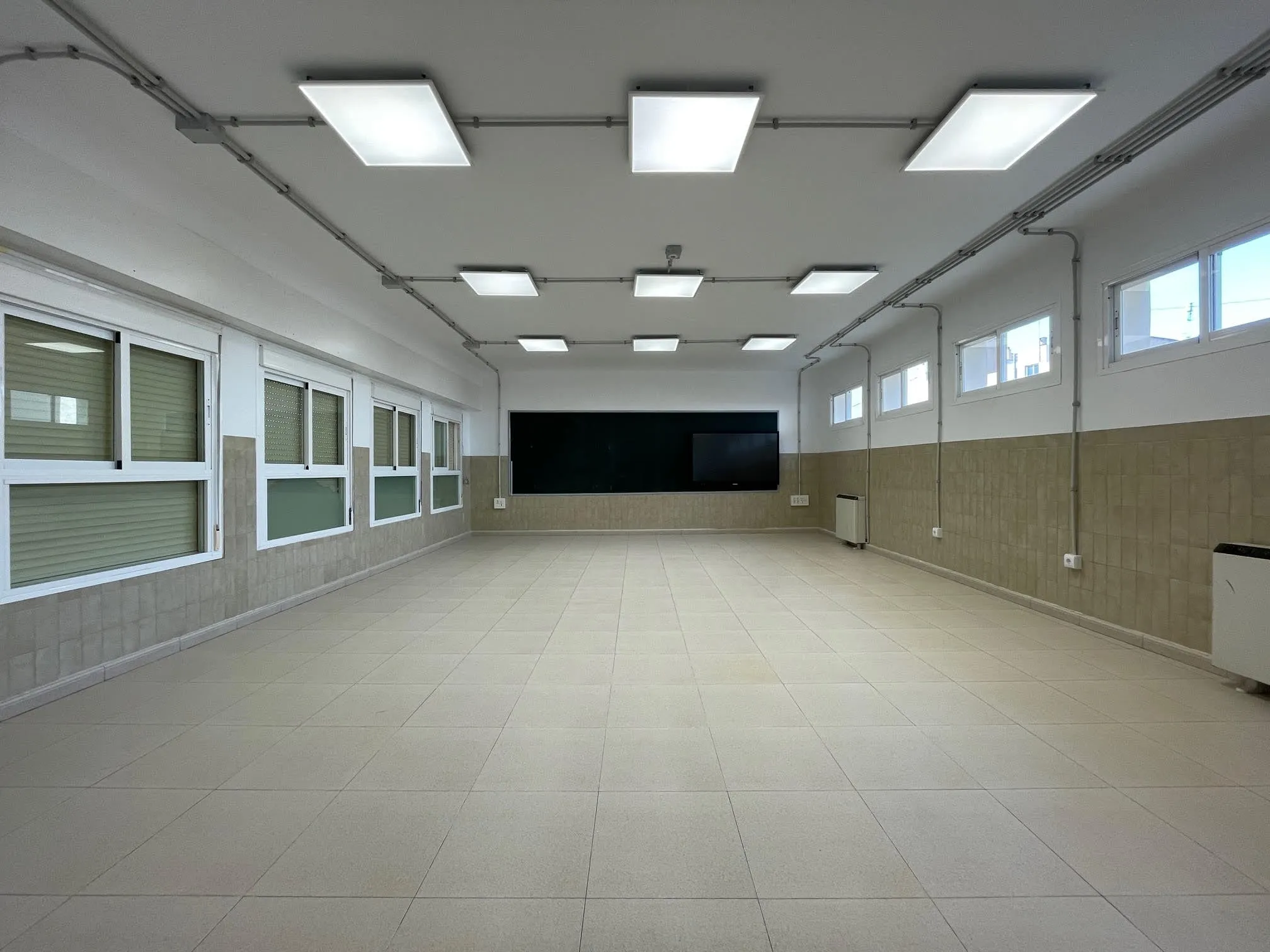 Aula diáfana con ventanas altas y zócalo cerámico