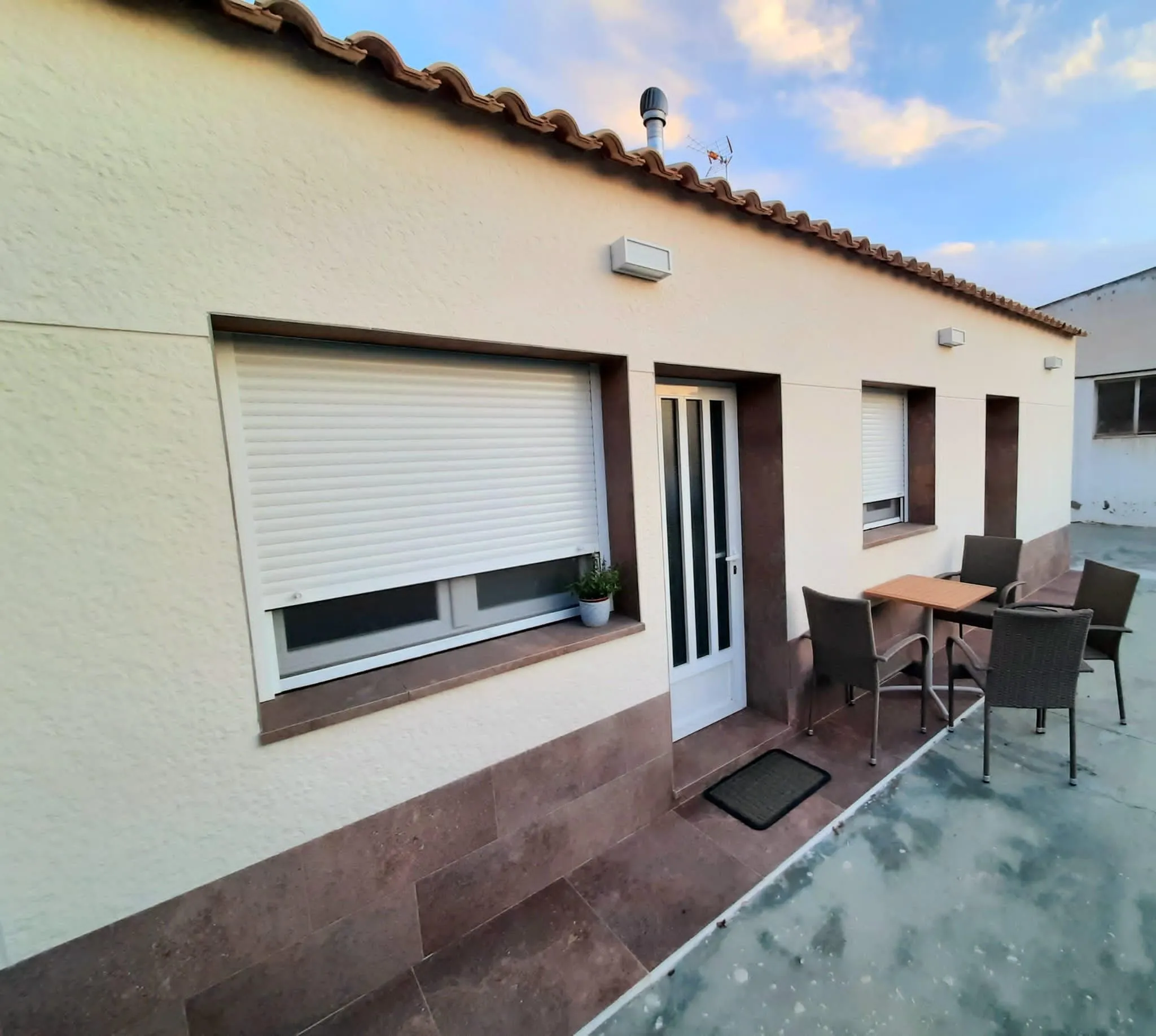 Terraza lateral pavimentada con mesa y sillas junto a la fachada