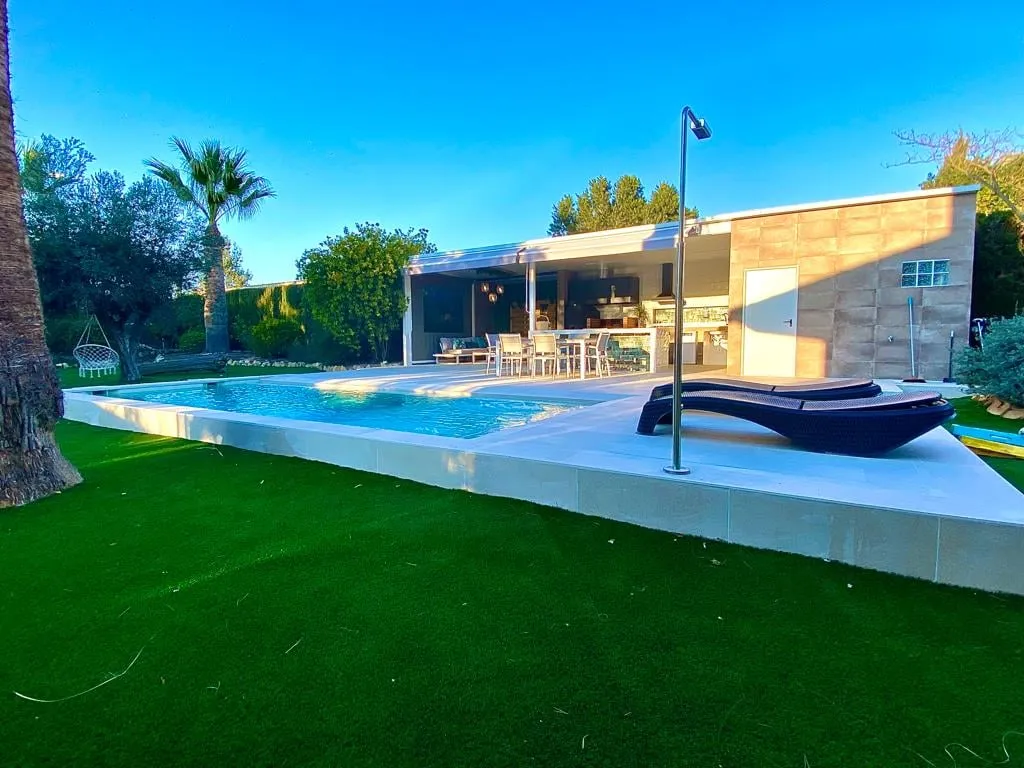Piscina junto a una gran pradera de césped con el porche al fondo